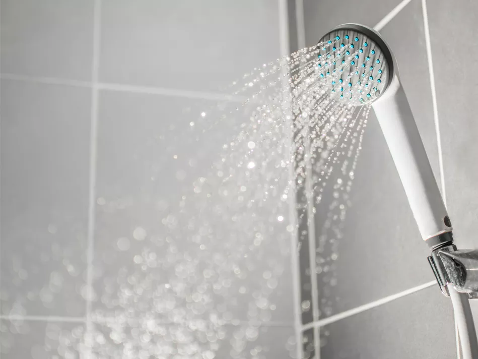 Water comes down from a white showerhead with blue nozzles that is mounted to a gray tiled bathroom wall