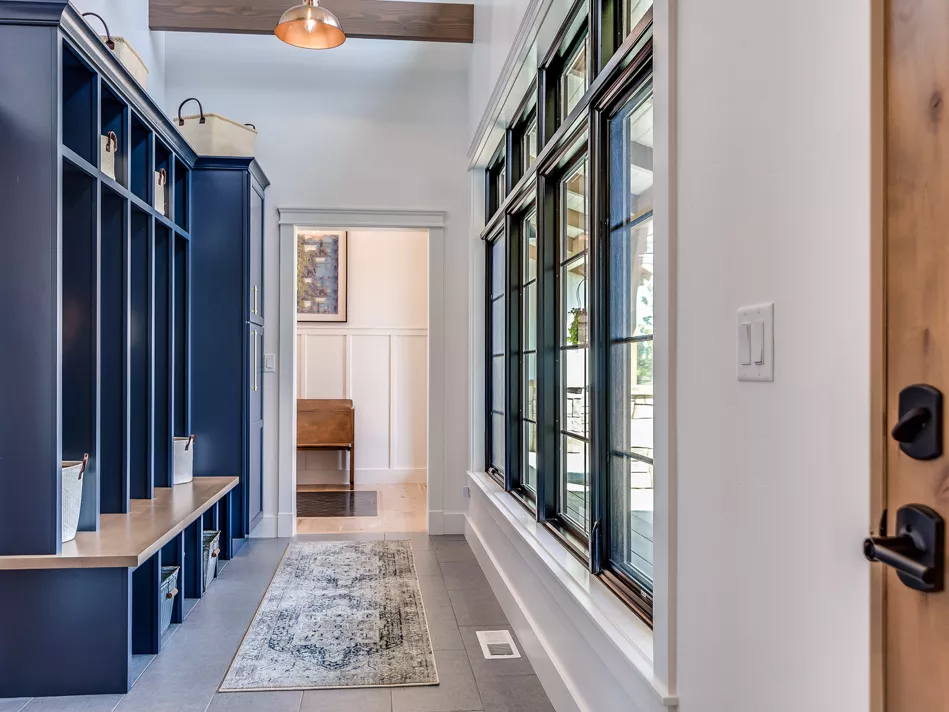 A mudroom with blue mudroom lockers, white walls, gray stone floors, and a pastel area rug
