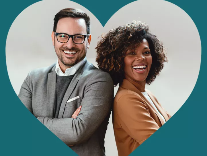 A white man and a Black woman stand back-to-back in business wear while smiling; they are on the inside of a heart-shaped cutout of a teal foreground